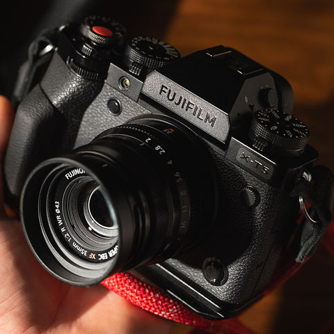 Hand holding a Fujifilm camera with a stealth label, red strap below